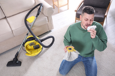 Photo of Man with vacuum cleaner bag suffering from dust allergy at home, above view