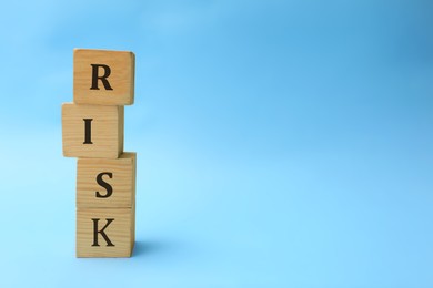 Photo of Stack of wooden cubes with word Risk on light blue background. Space for text