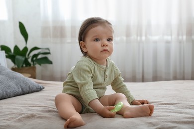 Photo of Cute baby girl with teething toy on bed at home