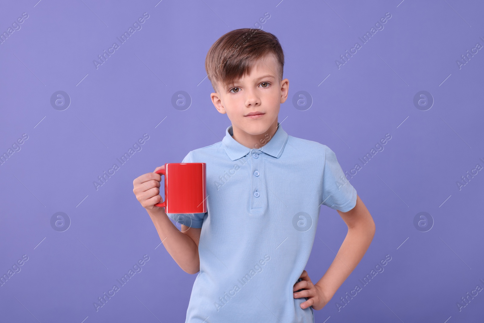 Photo of Cute boy with red ceramic mug on violet background