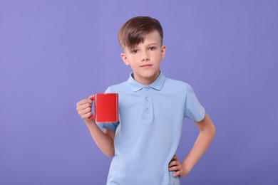 Cute boy with red ceramic mug on violet background