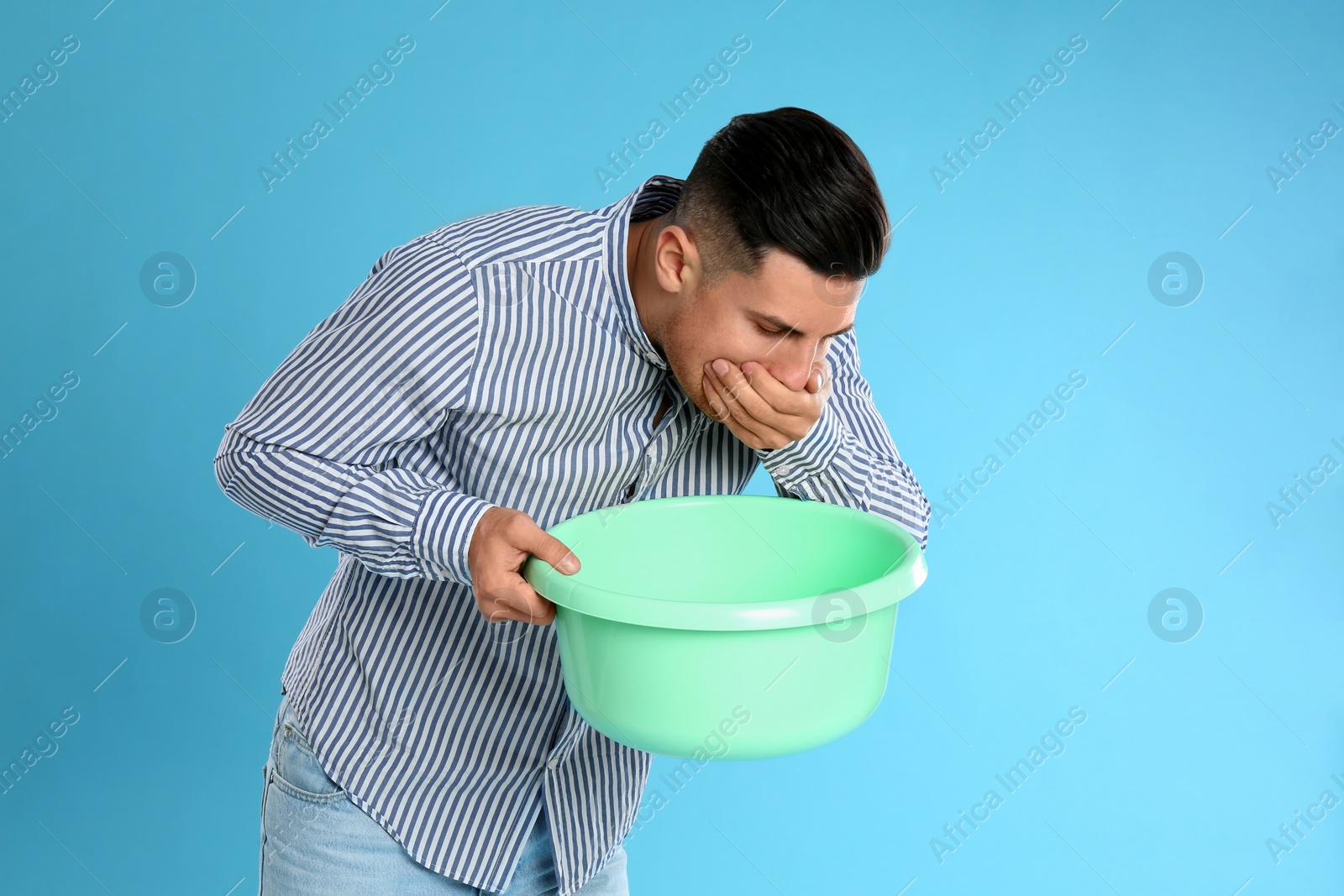 Photo of Man with basin suffering from nausea on light blue background. Food poisoning