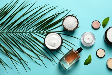 Photo of Different skin care cosmetic products with green leaves on color background, top view