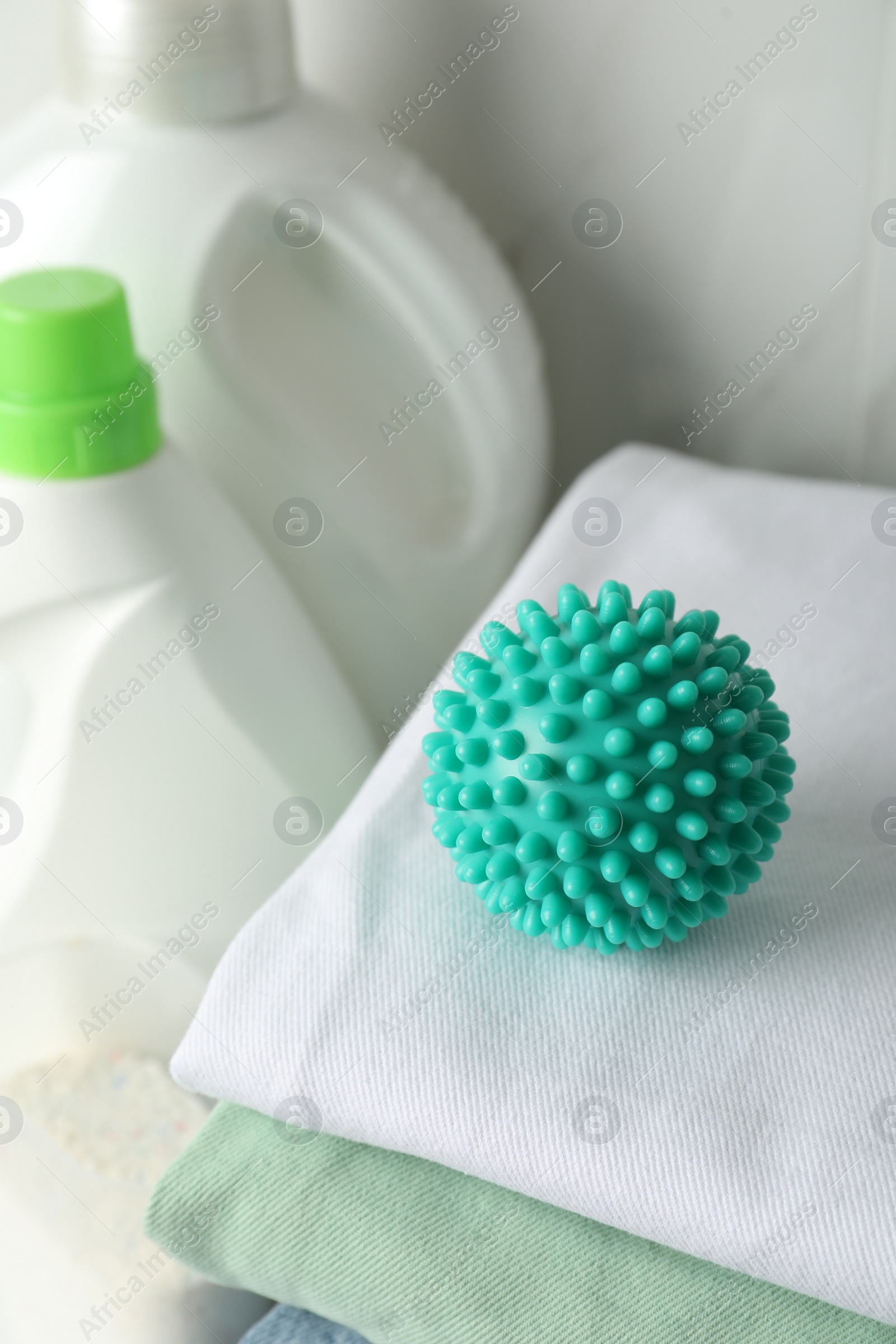 Photo of Turquoise dryer ball on stacked clean towels near laundry detergents