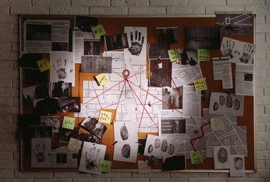 Photo of Detective board with fingerprints, photos, map and clues connected by red string on white brick wall