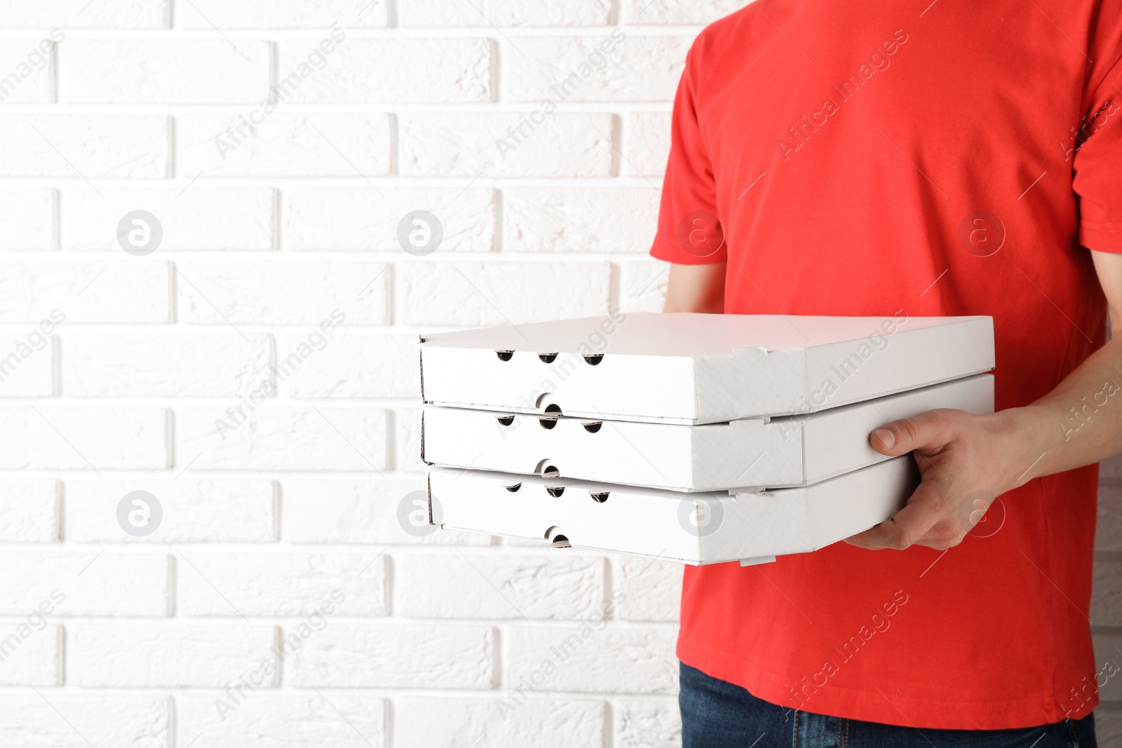 Photo of Young man with pizza boxes near white brick wall, space for text. Food delivery service