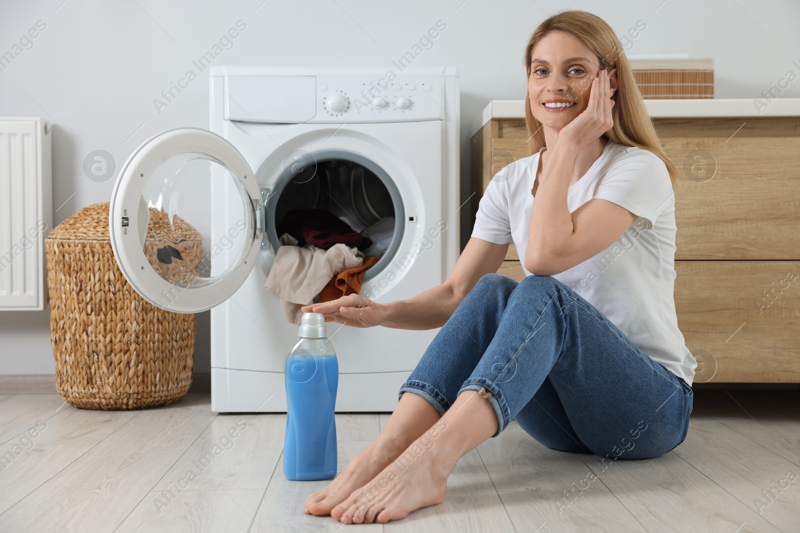 Photo of Woman sitting near washing machine and fabric softener in bathroom, space for text