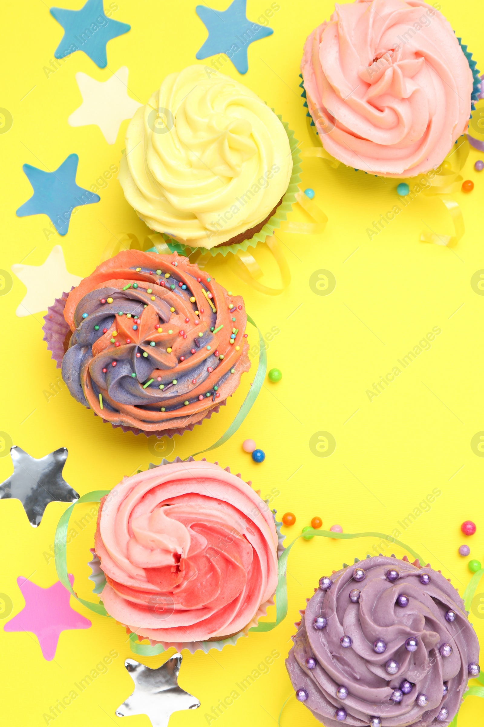 Photo of Delicious cupcakes with bright cream and party decor on yellow background, flat lay