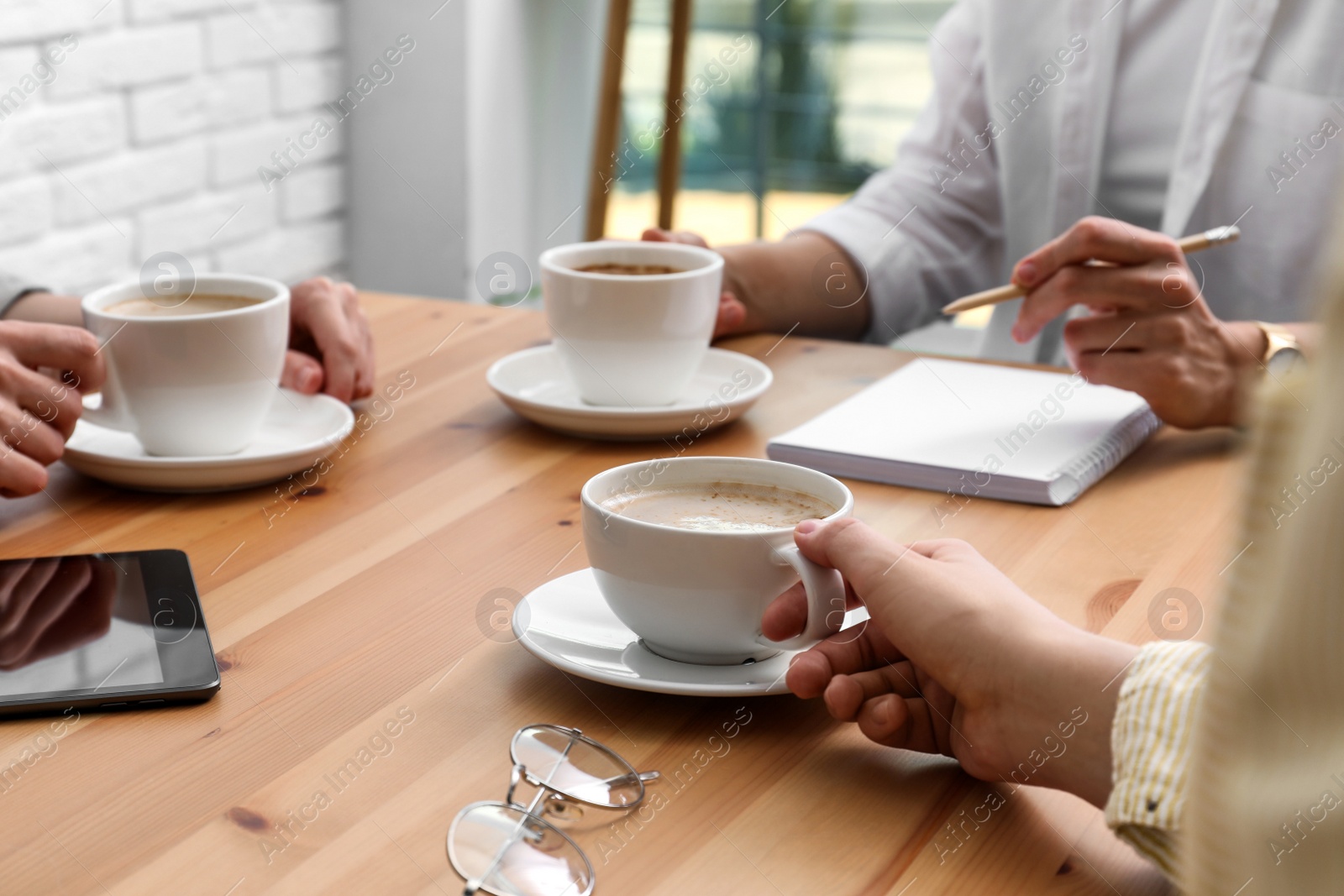 Photo of Women with cups of coffee at table in cafe, closeup