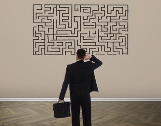Image of Businessman looking at wall with illustration of maze indoors