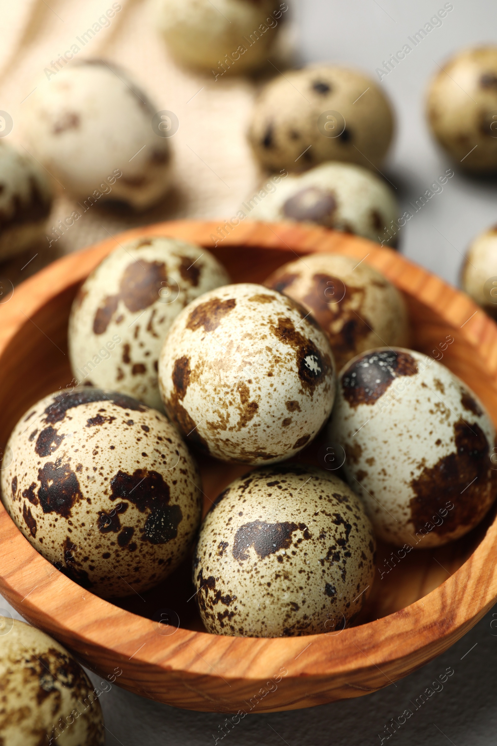 Photo of Wooden bowl and many speckled quail eggs on table, closeup