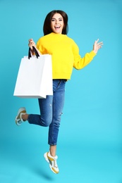 Happy young woman with paper bags jumping on blue background