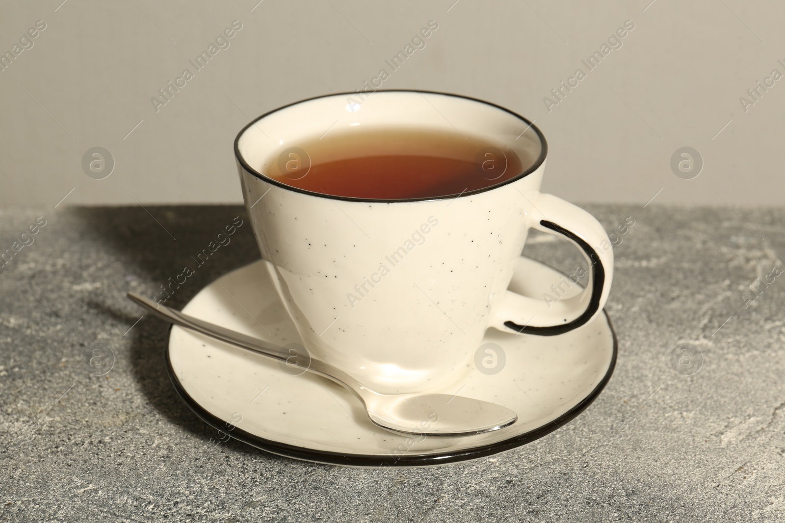 Photo of Aromatic tea in cup and spoon on grey table
