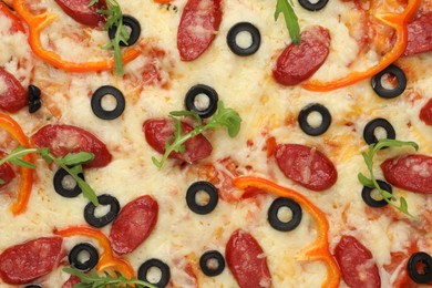 Photo of Tasty pizza with cheese, dry smoked sausages, olives, pepper and arugula as background, top view