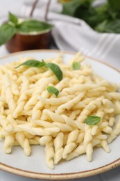 Photo of Plate of delicious trofie pasta with basil leaves on table, closeup