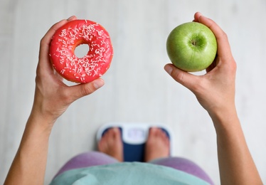 Photo of Choice concept. Top view of woman with apple and doughnut standing on scales, closeup