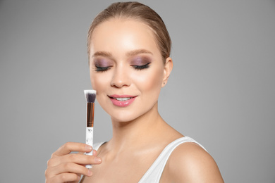 Photo of Beautiful woman applying makeup with brush on light grey background