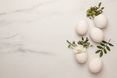 Photo of Easter eggs and beautiful flowers on white marble table, flat lay. Space for text