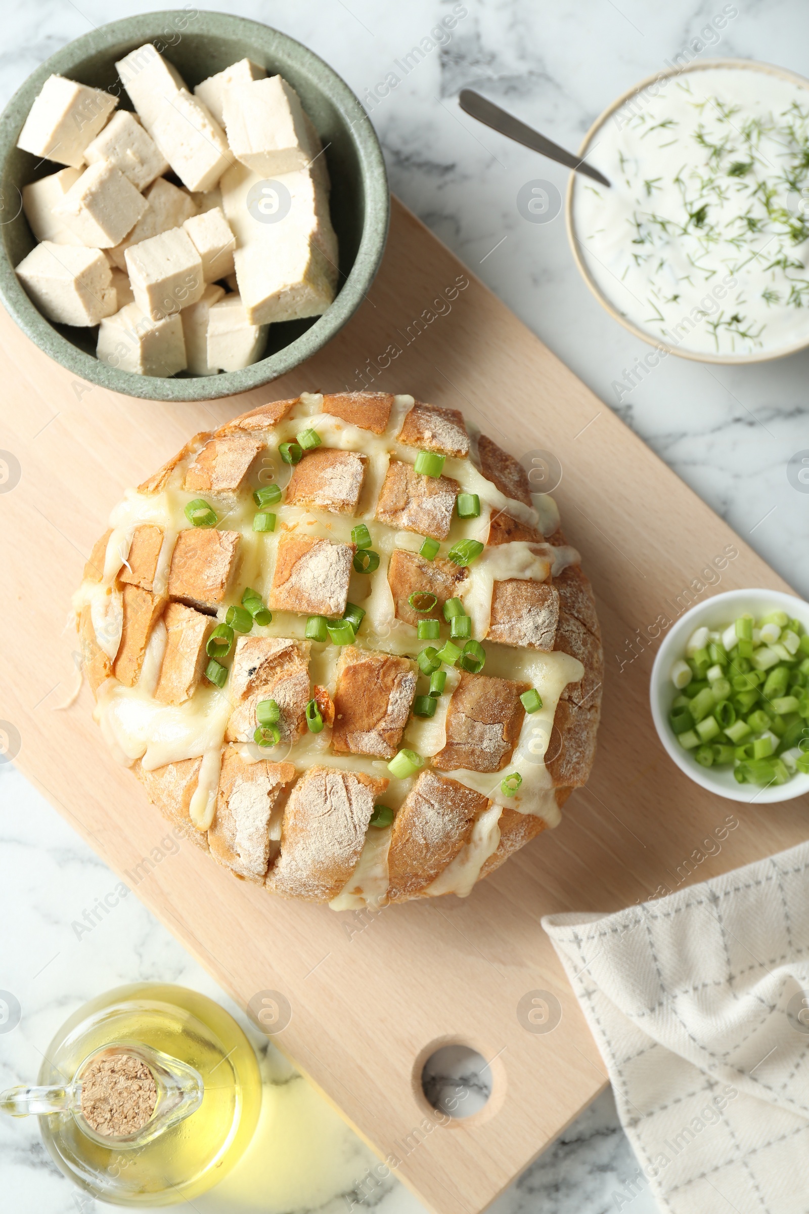 Photo of Freshly baked bread with tofu cheese and green onion served on white marble table, flat lay
