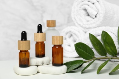 Photo of Bottles of essential oil, green leaves and spa stones on white table