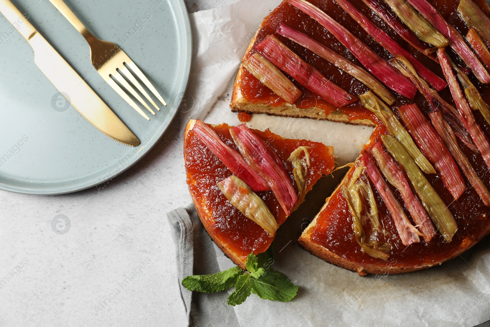 Photo of Freshly baked rhubarb pie and cutlery on light grey table, flat lay