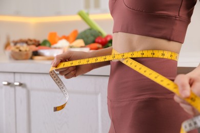 Photo of Woman with measuring tape in kitchen, closeup. Keto diet