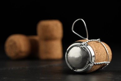 Photo of Sparkling wine cork with muselet cap on black table, closeup. Space for text