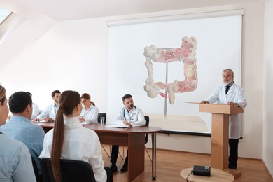 Image of Lecture in gastroenterology. Conference room full of professors and doctors. Projection screen with illustration of large intestine