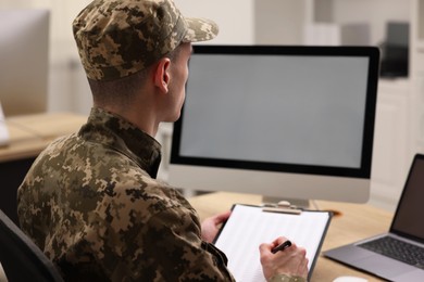 Photo of Military service. Soldier with clipboard working at table in office