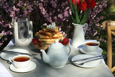 Beautiful bouquet of tulips and freshly baked waffles on table served for tea drinking in garden