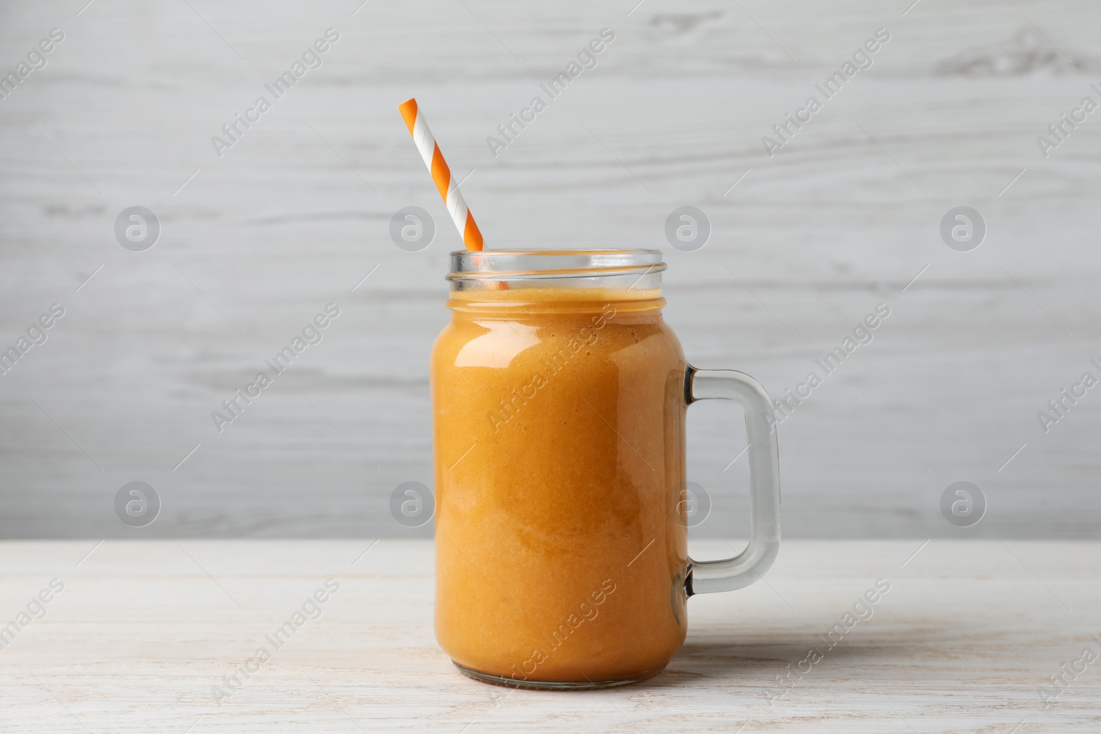 Photo of Mason jar with delicious fruit smoothie on white wooden table
