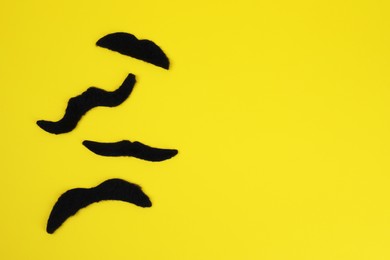 Photo of Different fake mustaches on yellow background, flat lay. Space for text