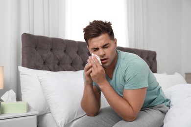 Photo of Young man suffering from allergy in bedroom