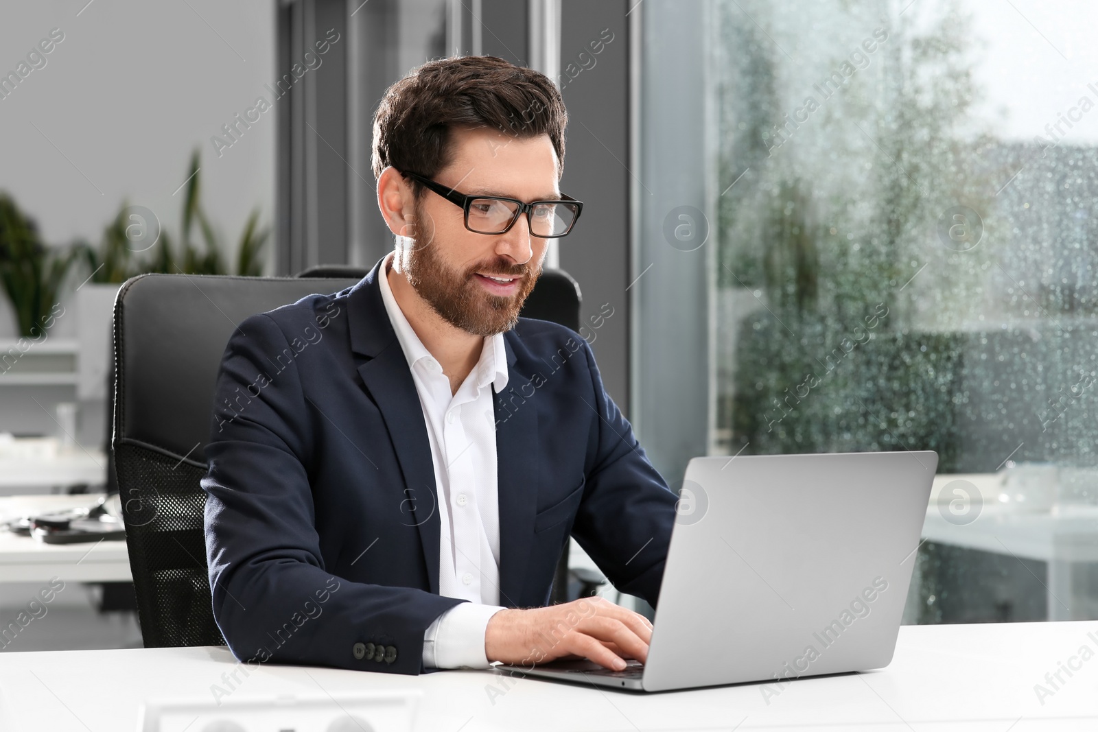 Photo of Man working on laptop at white desk in office