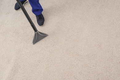 Photo of Man removing dirt from carpet with vacuum cleaner indoors, closeup. Space for text