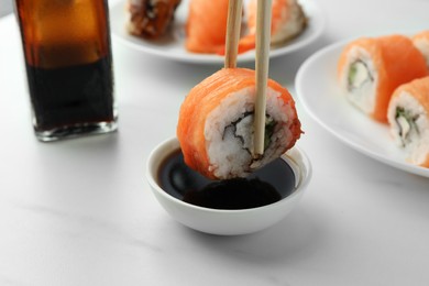 Photo of Dipping tasty sushi roll with salmon into soy sauce on white table, closeup