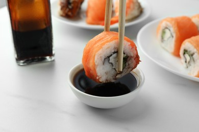 Dipping tasty sushi roll with salmon into soy sauce on white table, closeup