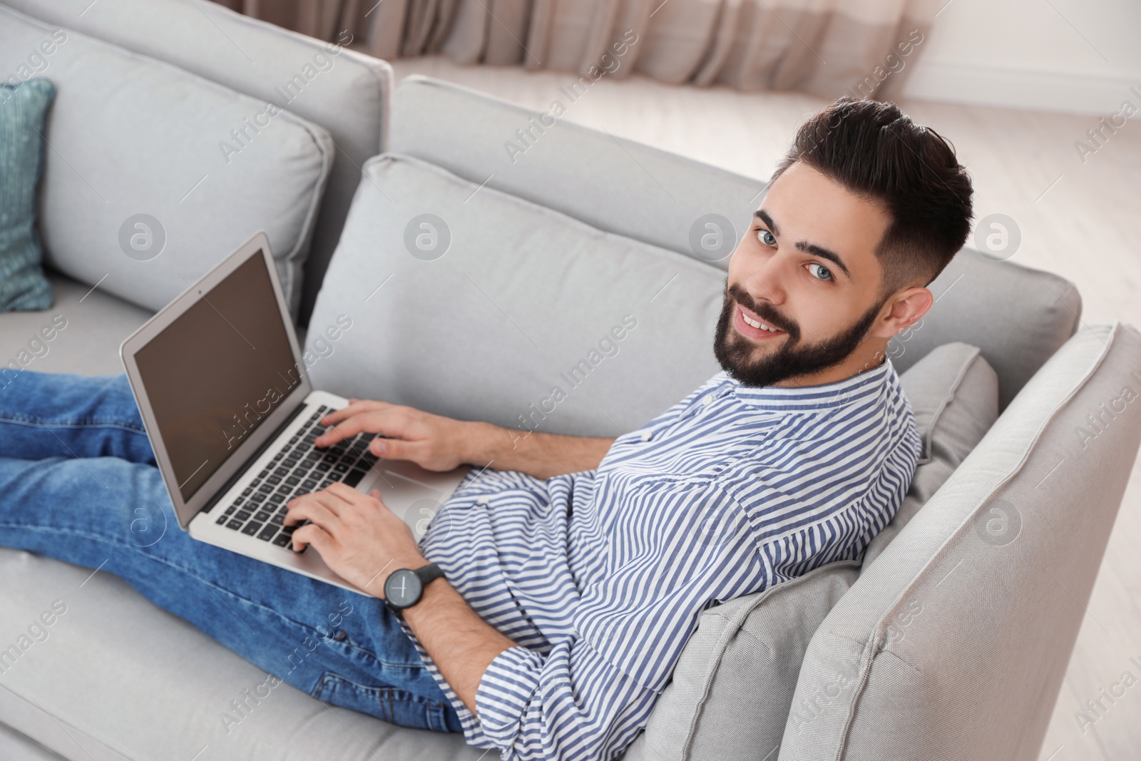 Photo of Handsome young man working with laptop on sofa at home