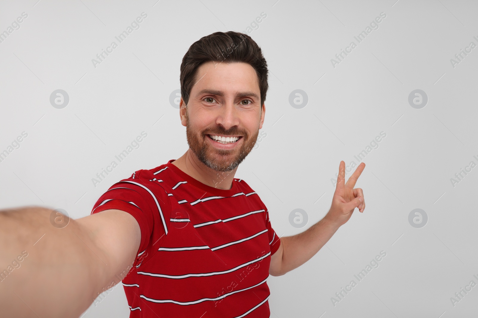 Photo of Smiling man taking selfie and showing peace sign on white background