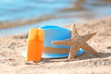 Photo of Starfish, bottle with sunscreen and hat on sand near sea. Beach object