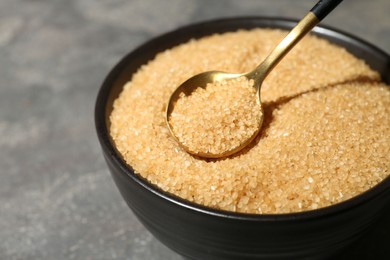 Photo of Taking brown sugar with spoon from bowl at grey table, closeup