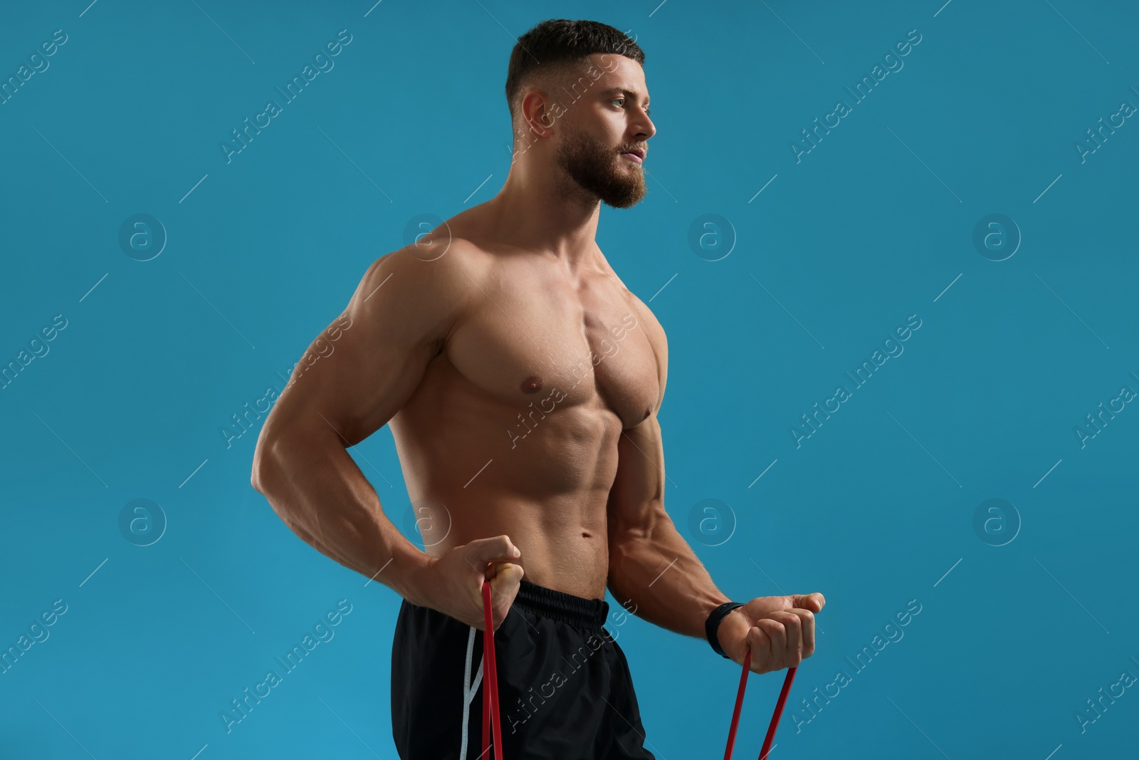 Photo of Muscular man exercising with elastic resistance band on light blue background