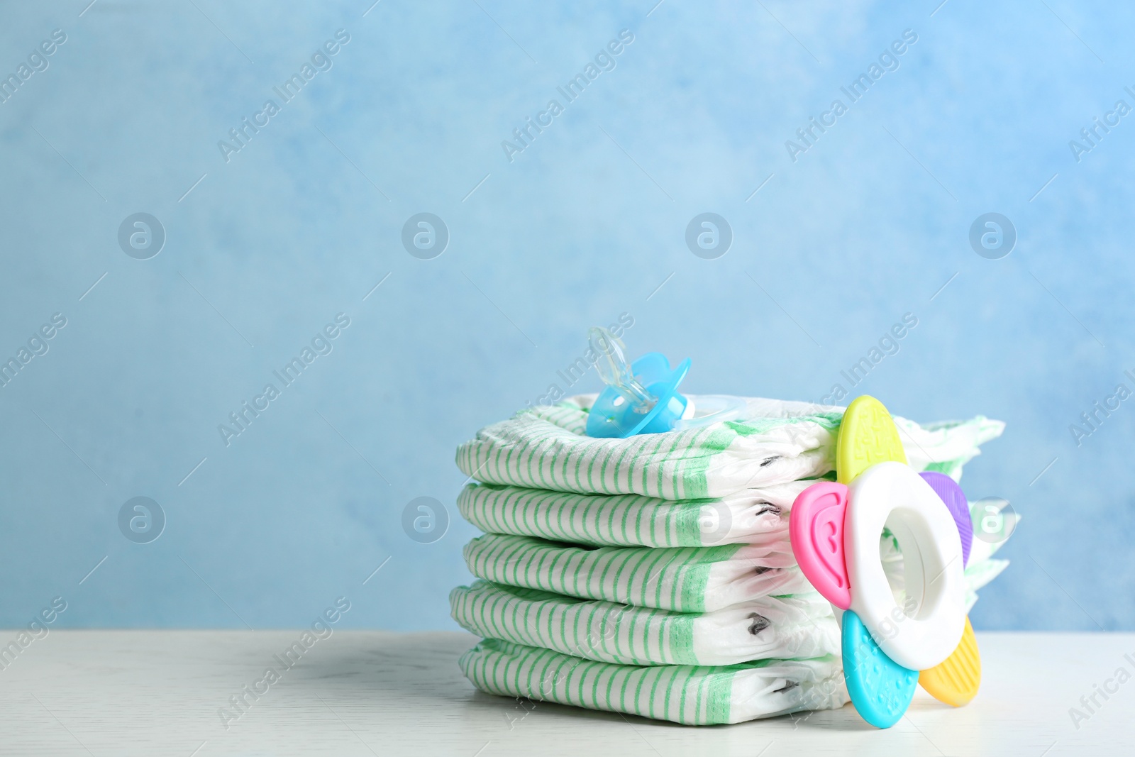 Photo of Stack of diapers and baby accessories on table against color background. Space for text
