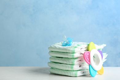 Photo of Stack of diapers and baby accessories on table against color background. Space for text