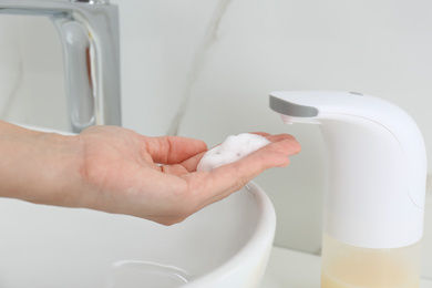 Woman using automatic soap dispenser in bathroom, closeup