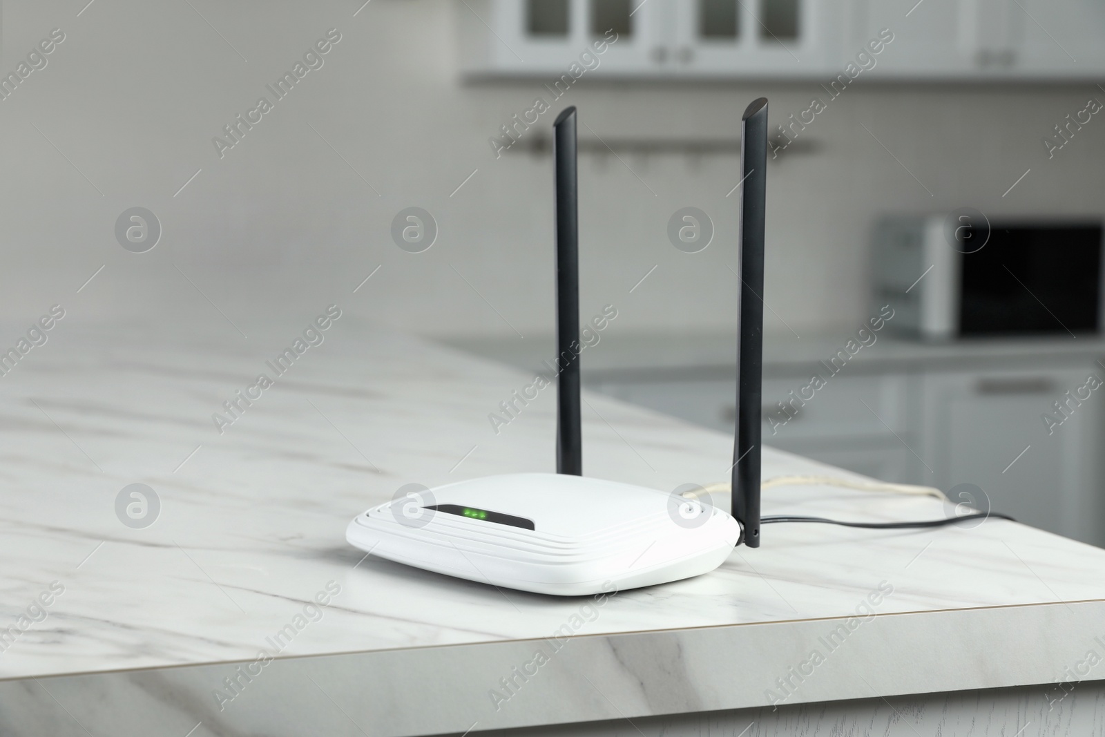 Photo of Modern Wi-Fi router on white marble table in kitchen