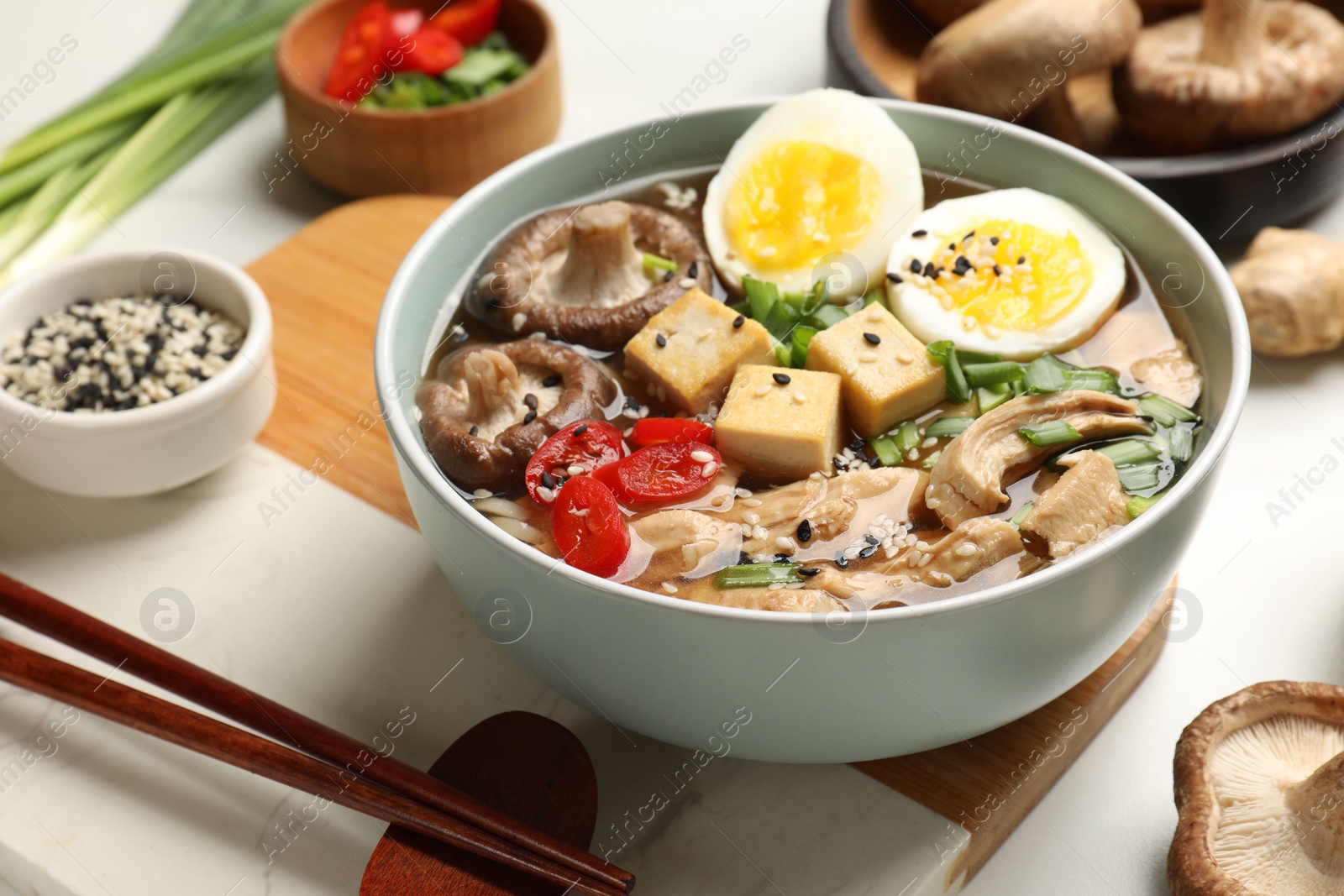 Photo of Bowl of delicious ramen and ingredients on white table. Noodle soup