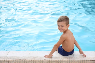 Cute little boy sitting near outdoor swimming pool