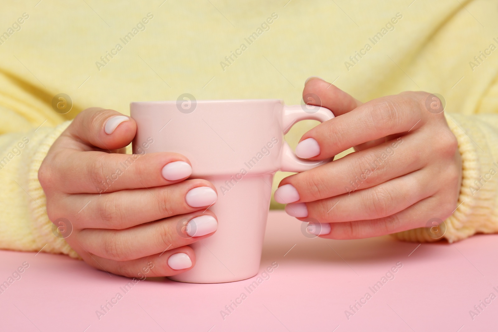 Photo of Woman with white nail polish holding cup at pink table, closeup