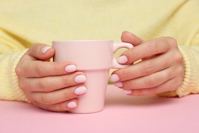 Woman with white nail polish holding cup at pink table, closeup